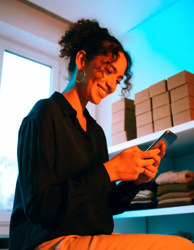 Emprendedora revisando los pedidos de su negocio en el teléfono, junto a cajas listas para enviar